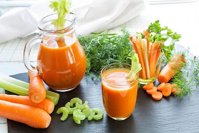 Fresh carrot juice with carrots, celery, dill and parsley on black background