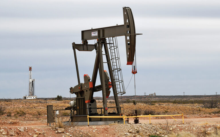 FILE PHOTO: A pump jack operates in front of a drilling rig owned by Exxon near Carlsbad