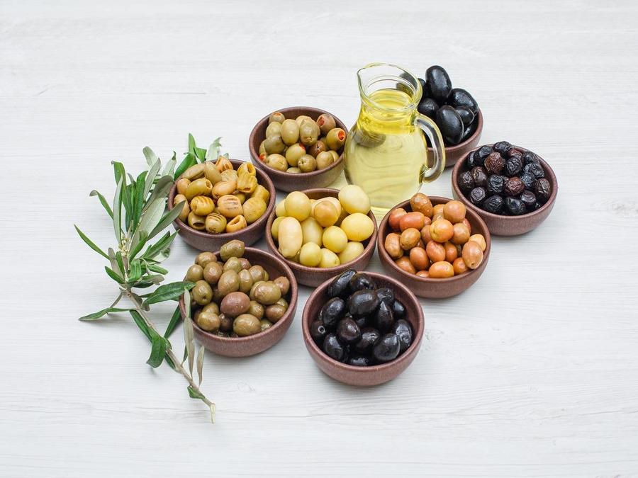 Assorted variety of olives in a clay bowls with olive leaves and a jar of olive oil high angle view on a white wooden background