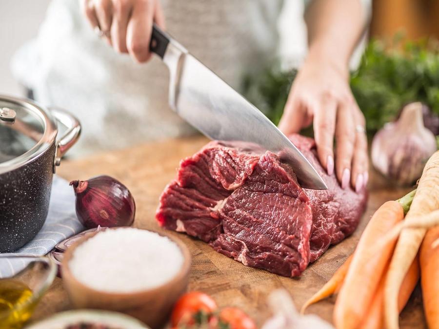 Young housewife slicing fresh beef steak. Female hands preparing lunch of meat and vegetables.
