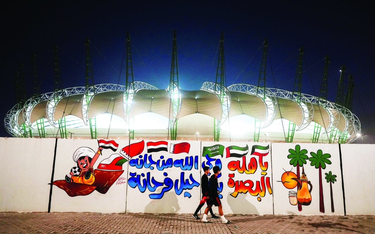 Iraqi men walk in front of Al-Minaa Olympic Stadium braces to host the Arabian Gulf Cup25, in Basra