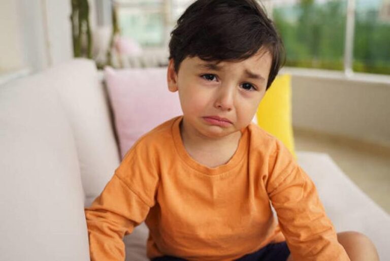 Portrait of crying innocent toddler boy sitting on a sofa at the balcony