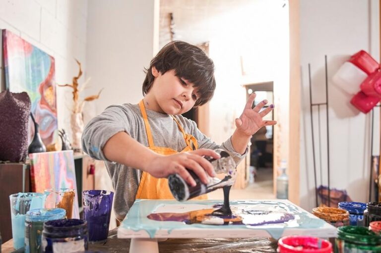 Inspired brunette boy drawing abstract painting with fluid art technique at the art school